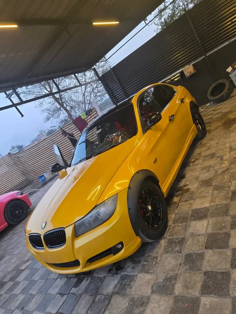 A yellow BMW 3 Series with black alloy wheels parked under the Car Doctor India canopy