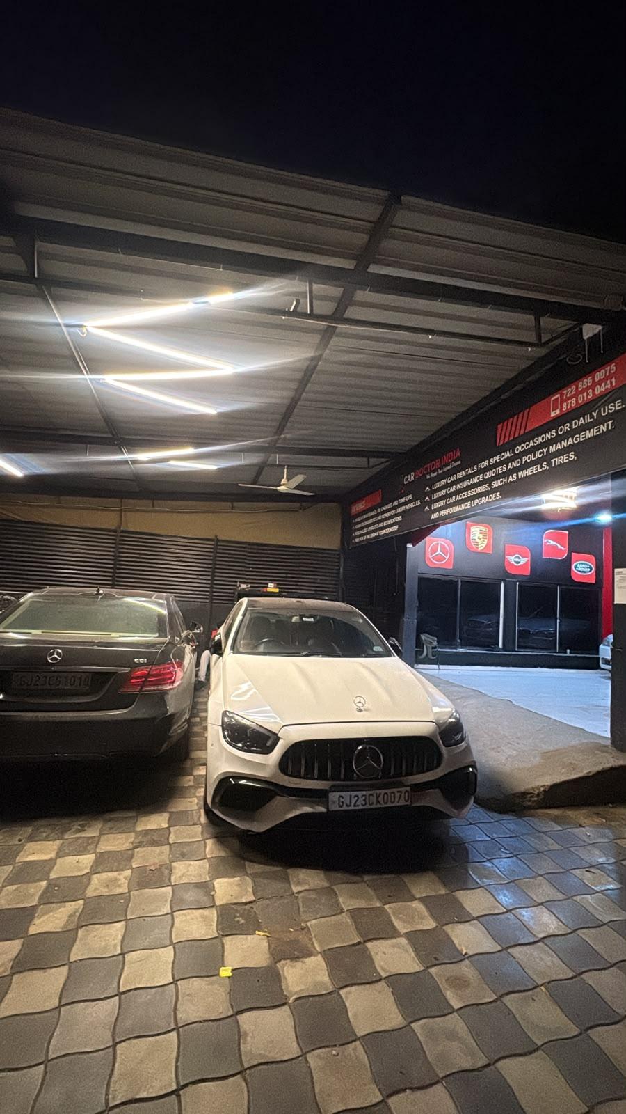 A white Mercedes-AMG and a dark Mercedes-Benz E-Class parked under the Car Doctor India canopy at night