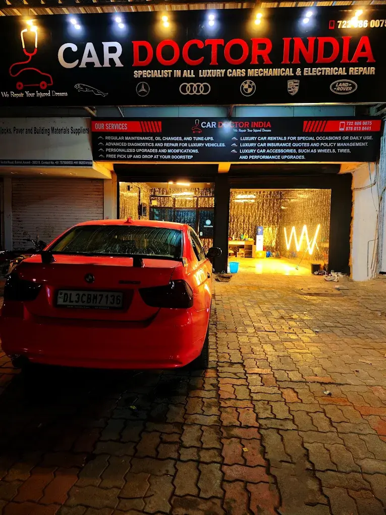 A red BMW parked beneath the illuminated Car Doctor India sign at night, with luxury marque badges displayed across the signage