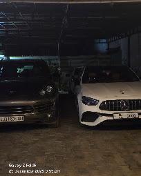 A dark Porsche Cayenne and a white Mercedes-AMG parked side by side inside the workshop at night